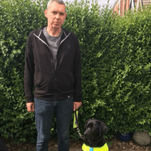 Richard Boggie with his guide dog, who is black and wearing a yellow harness.