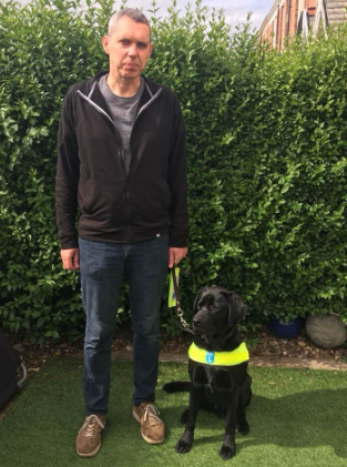 Richard with his guide dog, who is black and wearing a yellow harness.